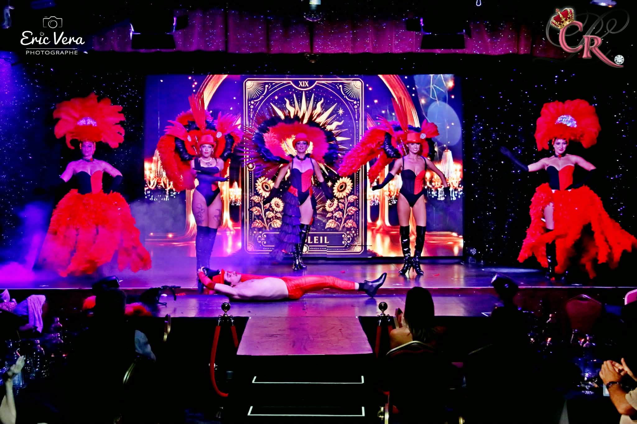 Artistes du Cabaret La Cour Royale sur scène en costumes rouges et noirs à plumes, sous un éclairage violet — photographie signée Éric Vera.